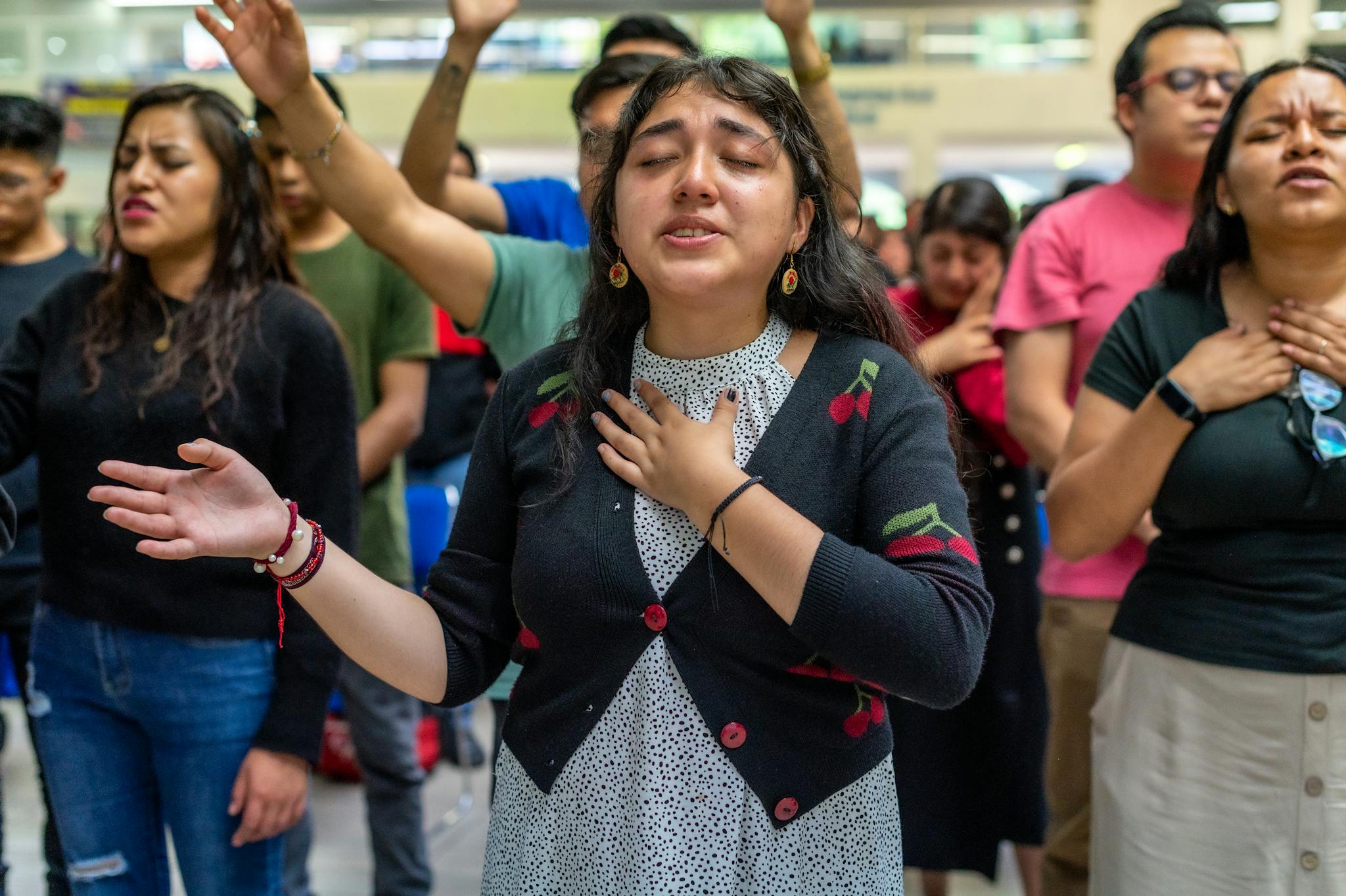 A diverse group of adults engaged in an emotional prayer during a public gathering.